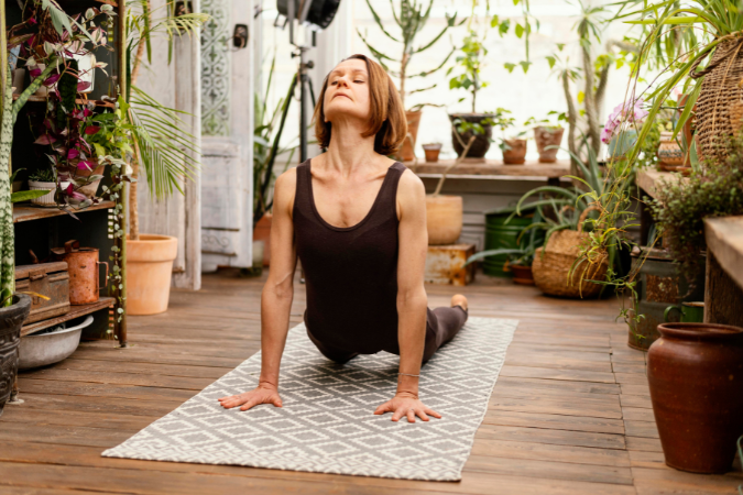 A woman is shown stretching on a yoga mat, possibly in a home or studio setting. The image reflects the physical aspect of yoga and the importance of stretching