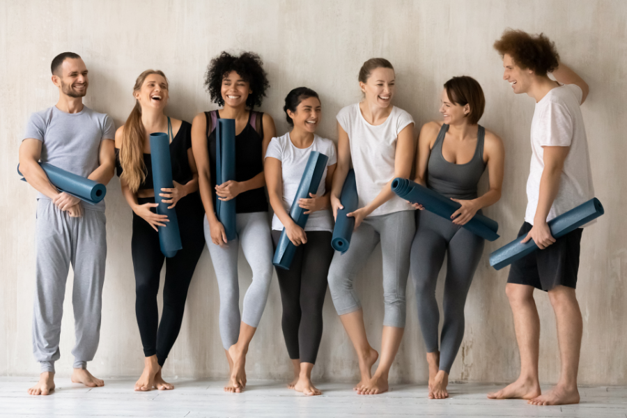 A group of seven people wearing different styles of activewear, holding yoga mats and smiling, ready for a yoga session. This image showcases the diversity and comfort of activewear.