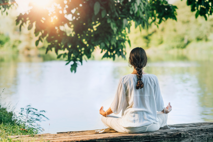 A person meditating by a lake in a calm, serene environment, wearing comfortable yoga apparel.