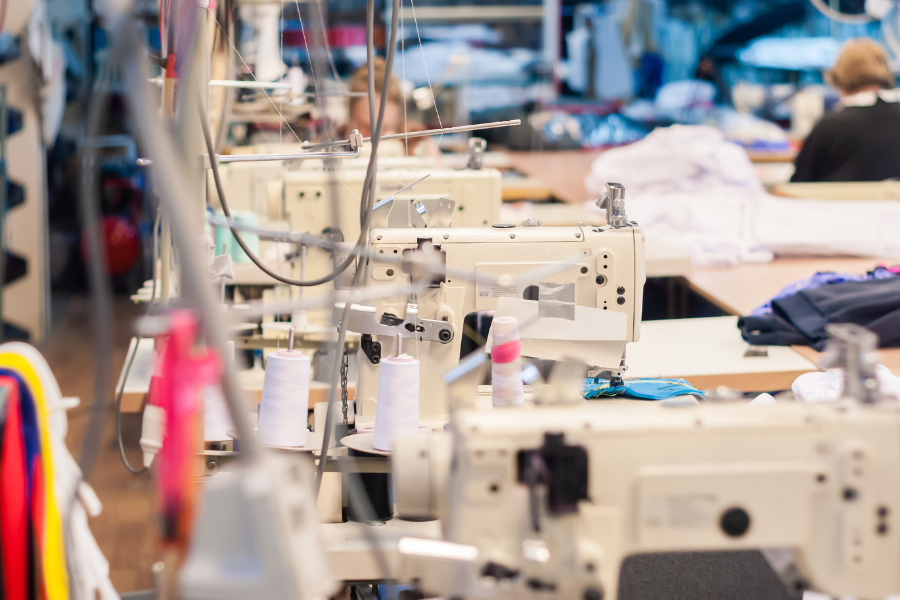 Sewing machines in a factory setting, showcasing the process of manufacturing activewear, with spools of thread and workers preparing garments for stitching.