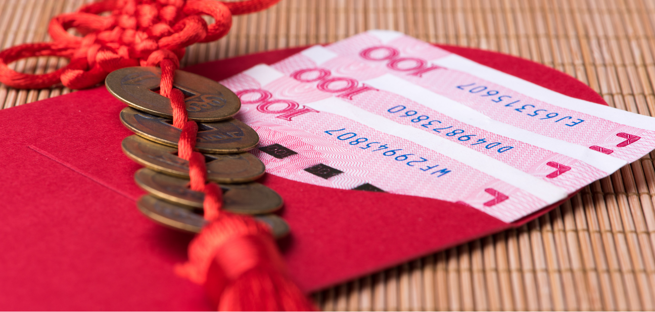 The image shows a red envelope with three 100 Chinese yuan banknotes partially visible inside it. Next to the envelope, there is a string of traditional Chinese coins tied together with a red cord. The background consists of a bamboo mat.