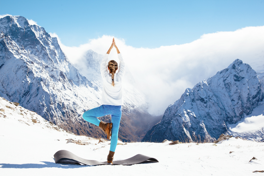 A person practicing yoga outdoors on a snowy mountain, showing winter yoga apparel in a breathtaking landscape.